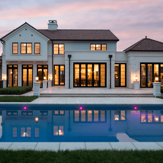 Classic white home with pool dimly lit at dusk
